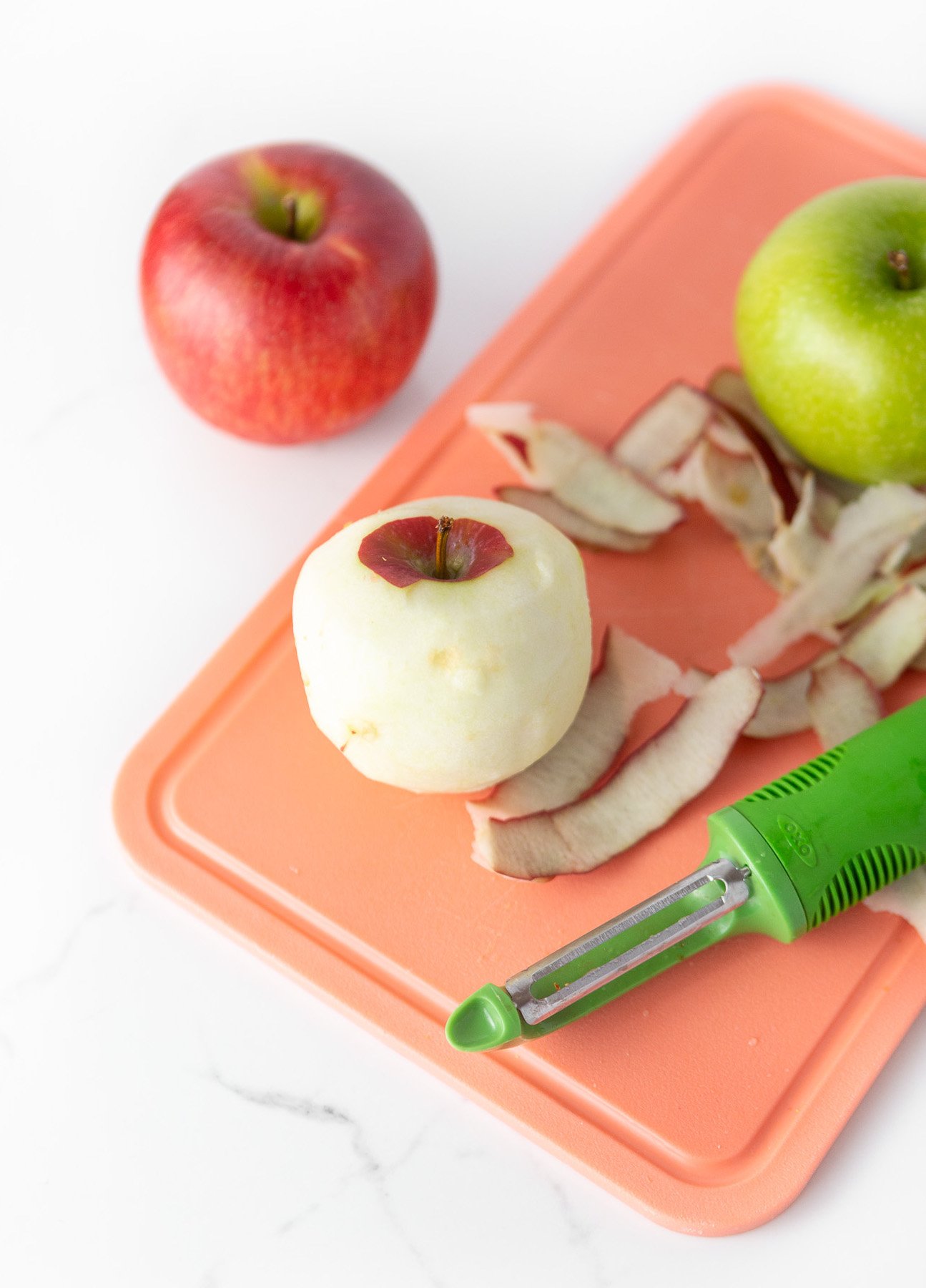 Pink cutting board peeling red and green apples
