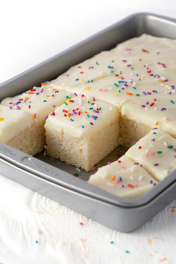 white sheet cake in metal 9x13 pan with white frosting and sprinkles