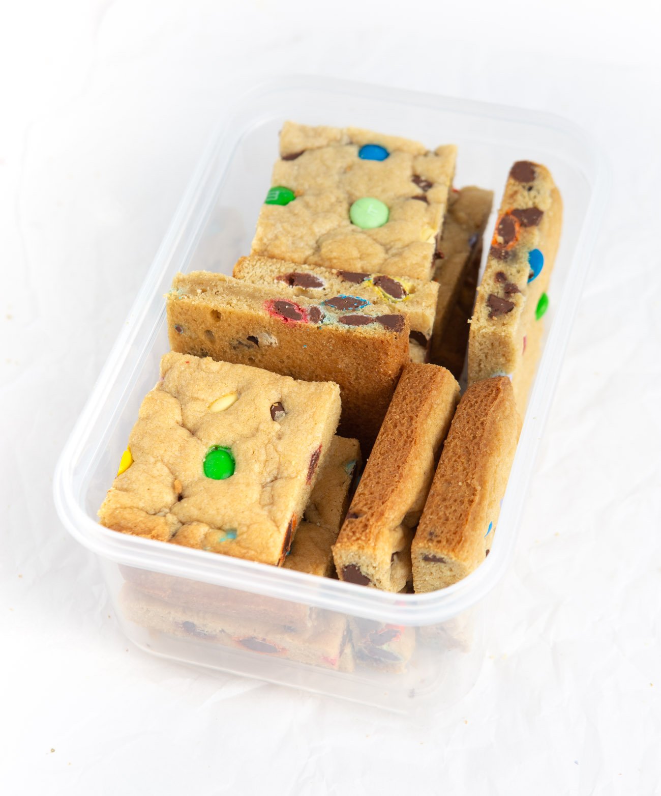 Chewy M&M Cookie bars cut into squares in plastic container for freezing