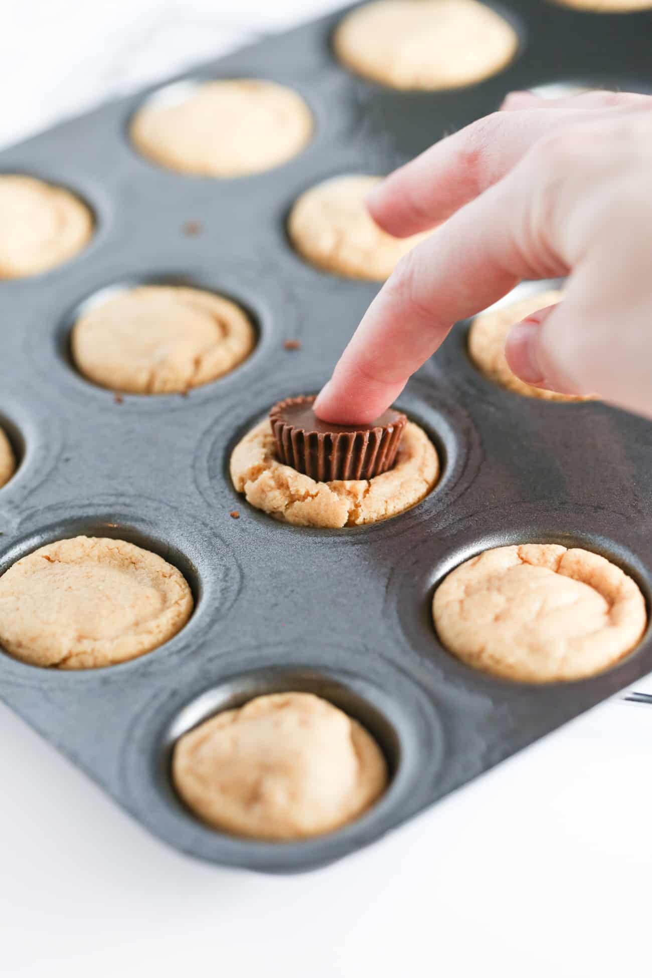 Finger pressing mini Reeses peanut butter cup into cookie muffin to make easy Christmas holly cookie cups!