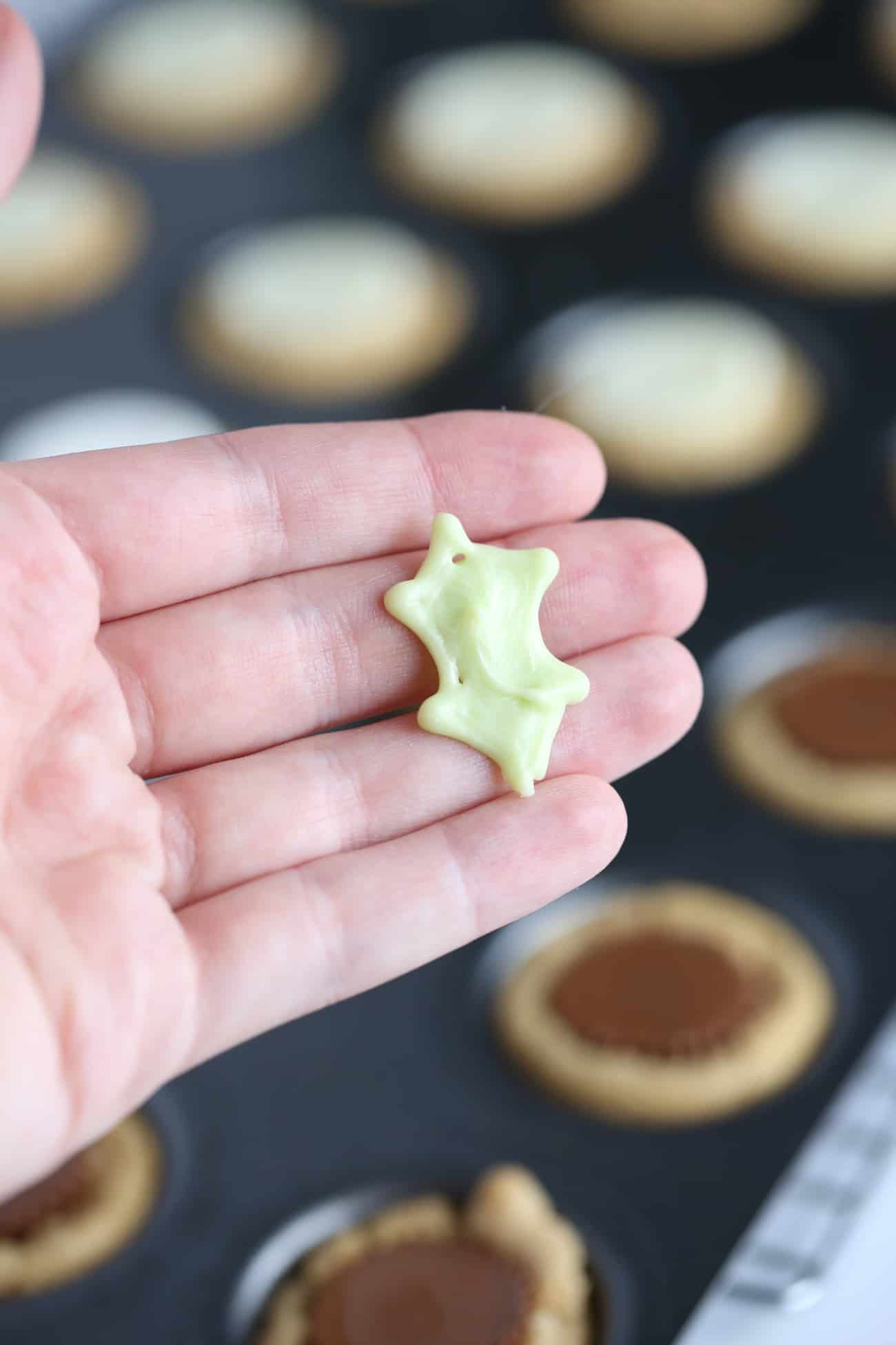 Hand holding white chocolate green holly leaf to make Holly leaf printable template to make easy Christmas holly cookie cups!