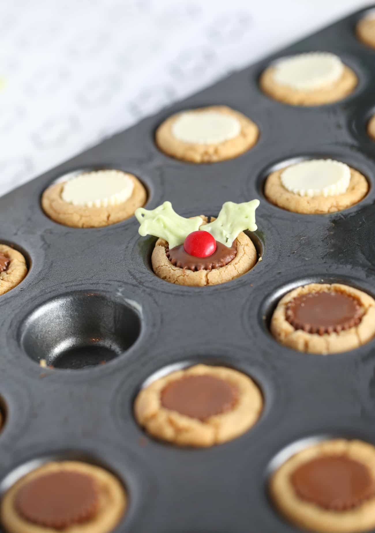 Mini muffin tin with peanut butter cookie cups to make easy Christmas holly cookie cups.