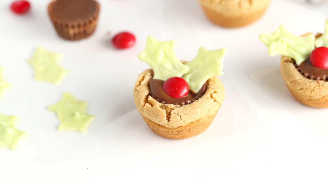 Reeses peanut butter cup cookie decorated like holly leaf to make easy Christmas holly cookie cups.