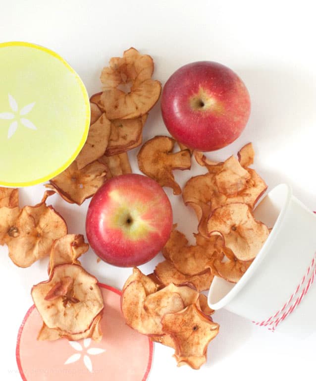 Baked apple chips on table coming out of paper cup for cute packaging idea.