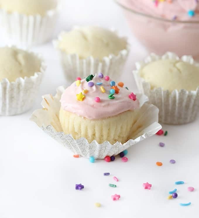 white cupcake with pink frosting and sprinkles in cupcake liner