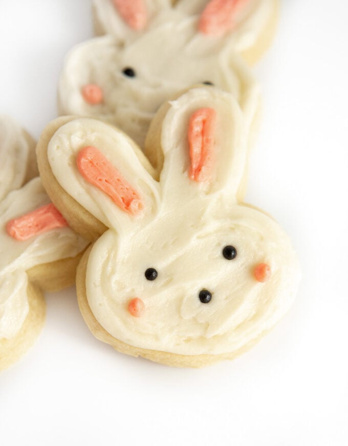 Bunny shaped sugar cookie decorated with white and pink frosting and black pearl sprinkles for eyes