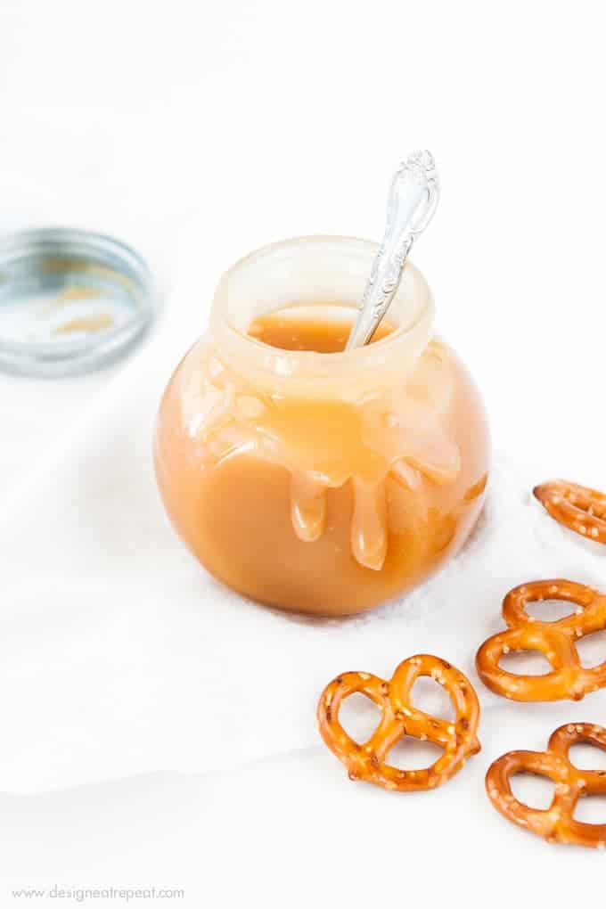 Jar of Salted Caramel Sauce with caramel dripping down sides. Pretzels for dipping.