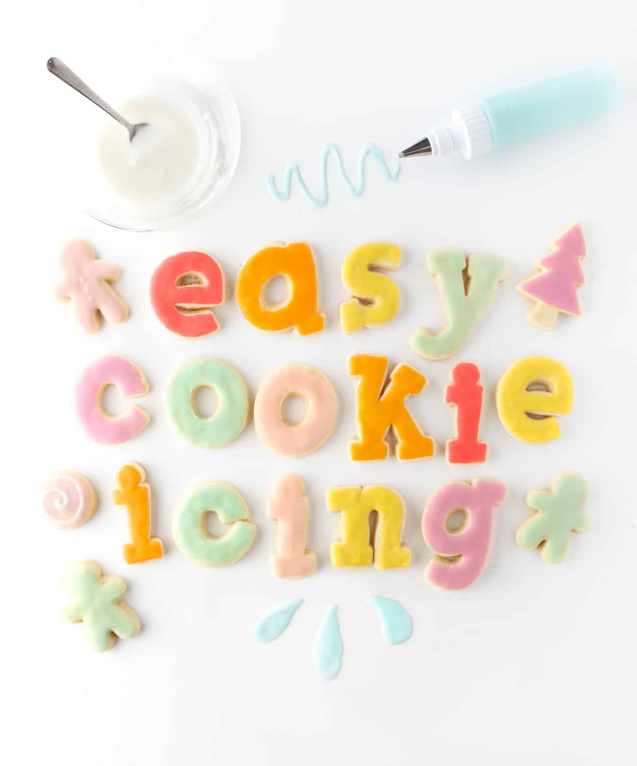 Rainbow sugar cookies spelling out the words Easy Sugar Cookie Icing. White bowl of icing with bottle of blue icing.