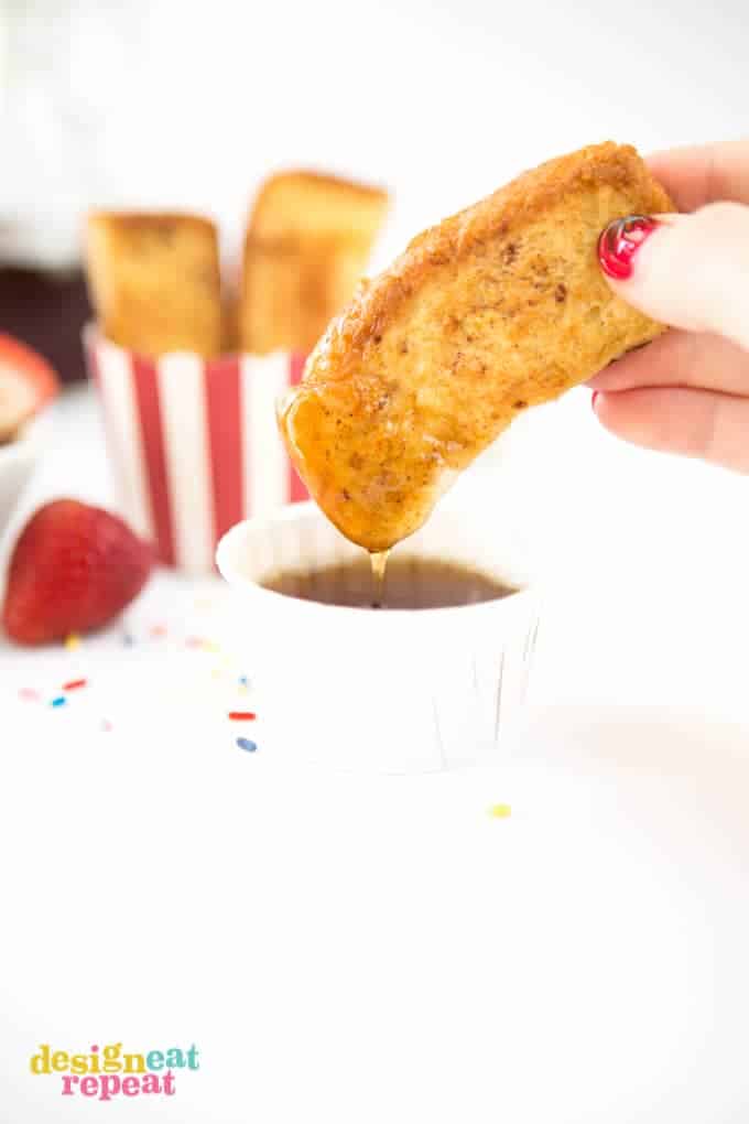 Hand dunking french toast stick into syrup