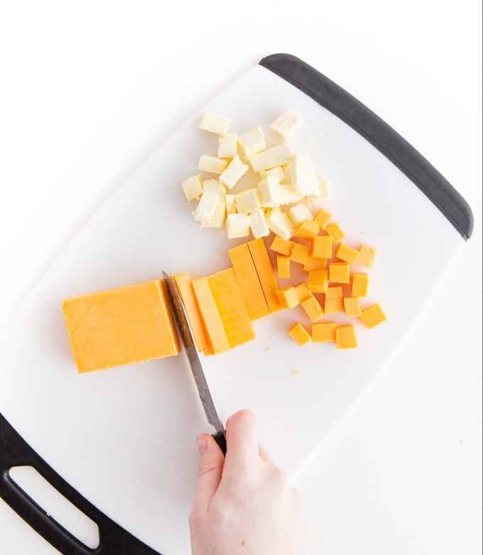 Cutting cheese and butter in small cubes with knife on cutting board to make homemade cheese crackers