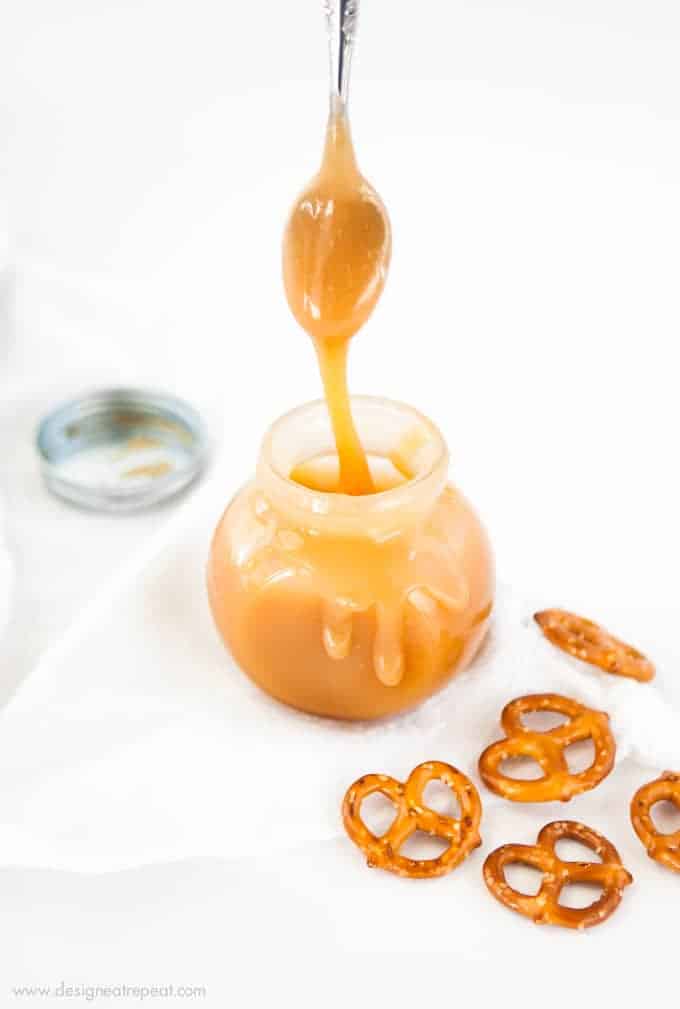 Jar of Homemade Microwave Salted Caramel Sauce with spoon and pretzels.