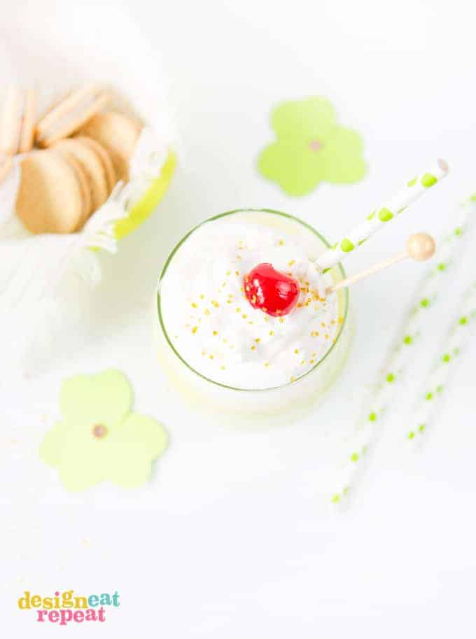 Mint Shamrock milkshake in glass cup topped with whipped cream, a cherry, and gold sprinkles.