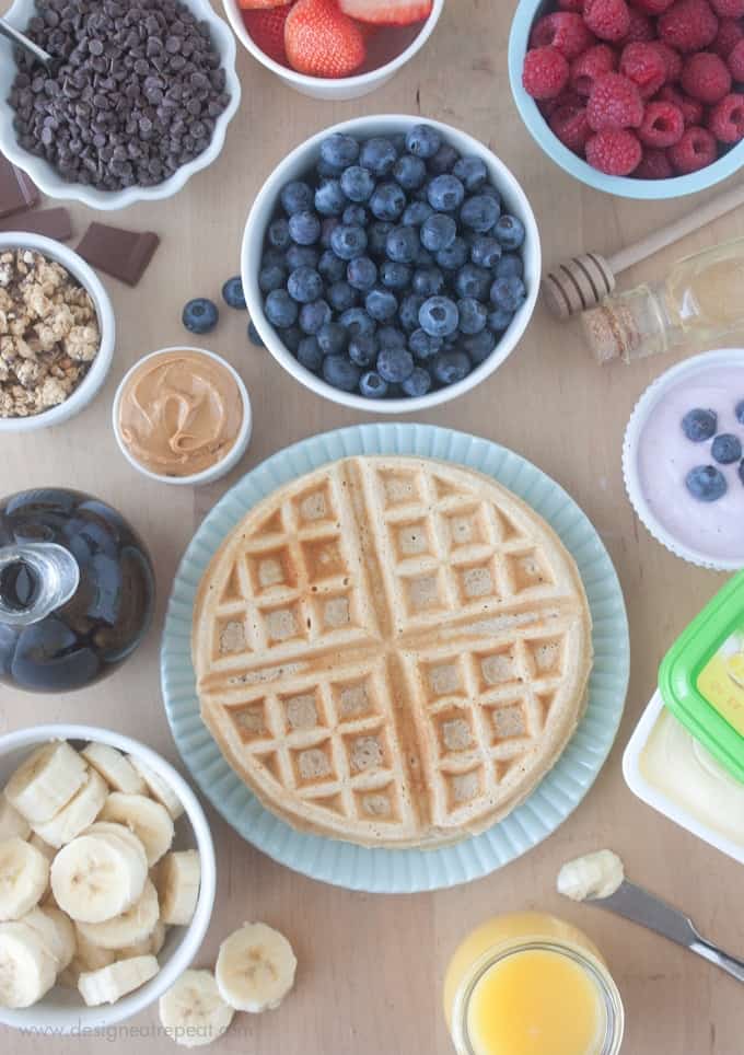 Overhead picture of waffle bar with waffle toppings. Blueberries, raspberries, peanut butter, bananas, and more.
