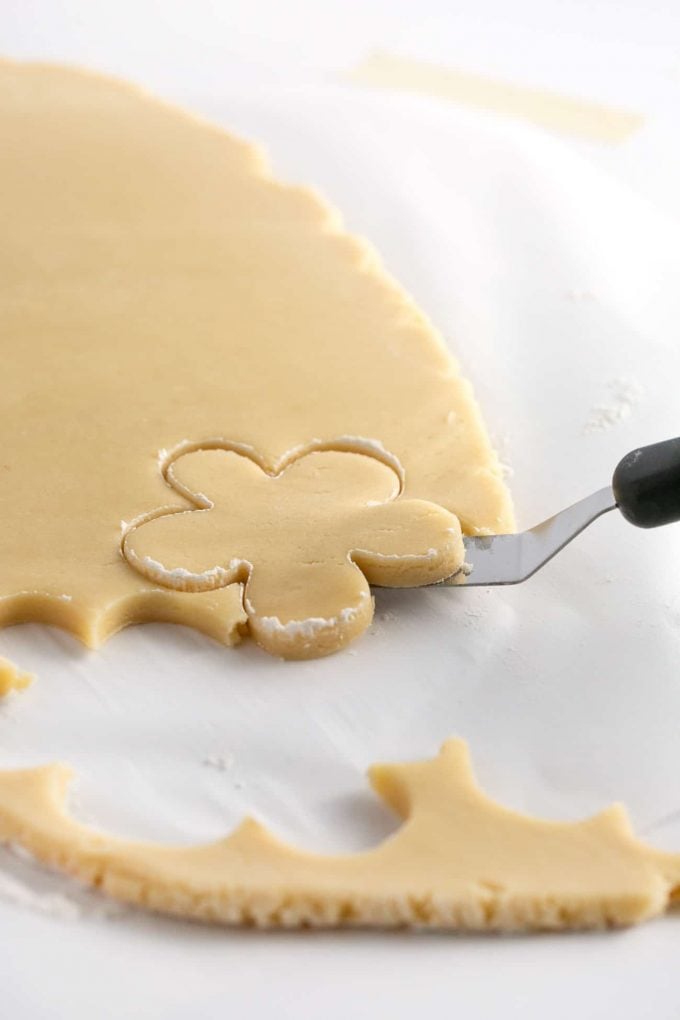Lifting cut flower sugar cookie dough off of parchment paper with offset spatula