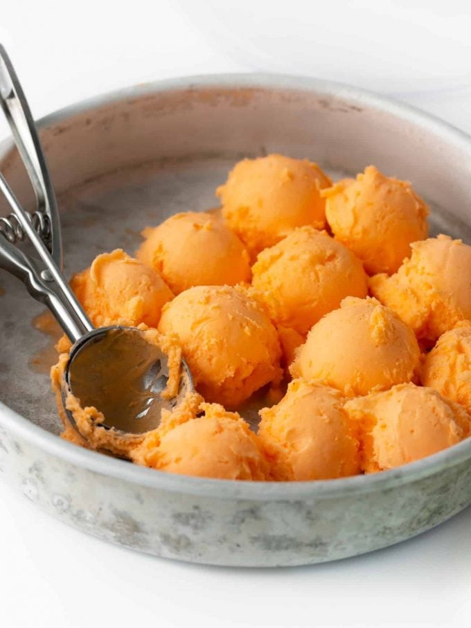 Scoops of orange sherbet punch in metal baking pan with ice cream scoop