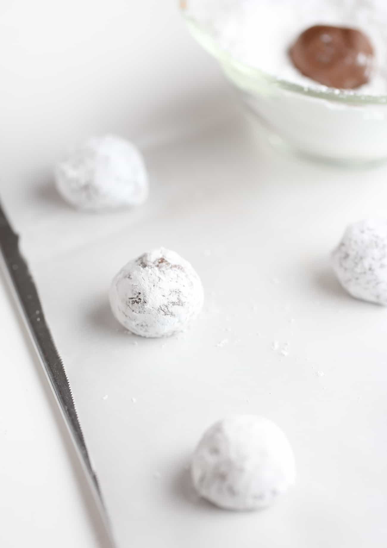 Balls of chocolate brownie cookies rolled in powdered sugar on cookie sheet. 