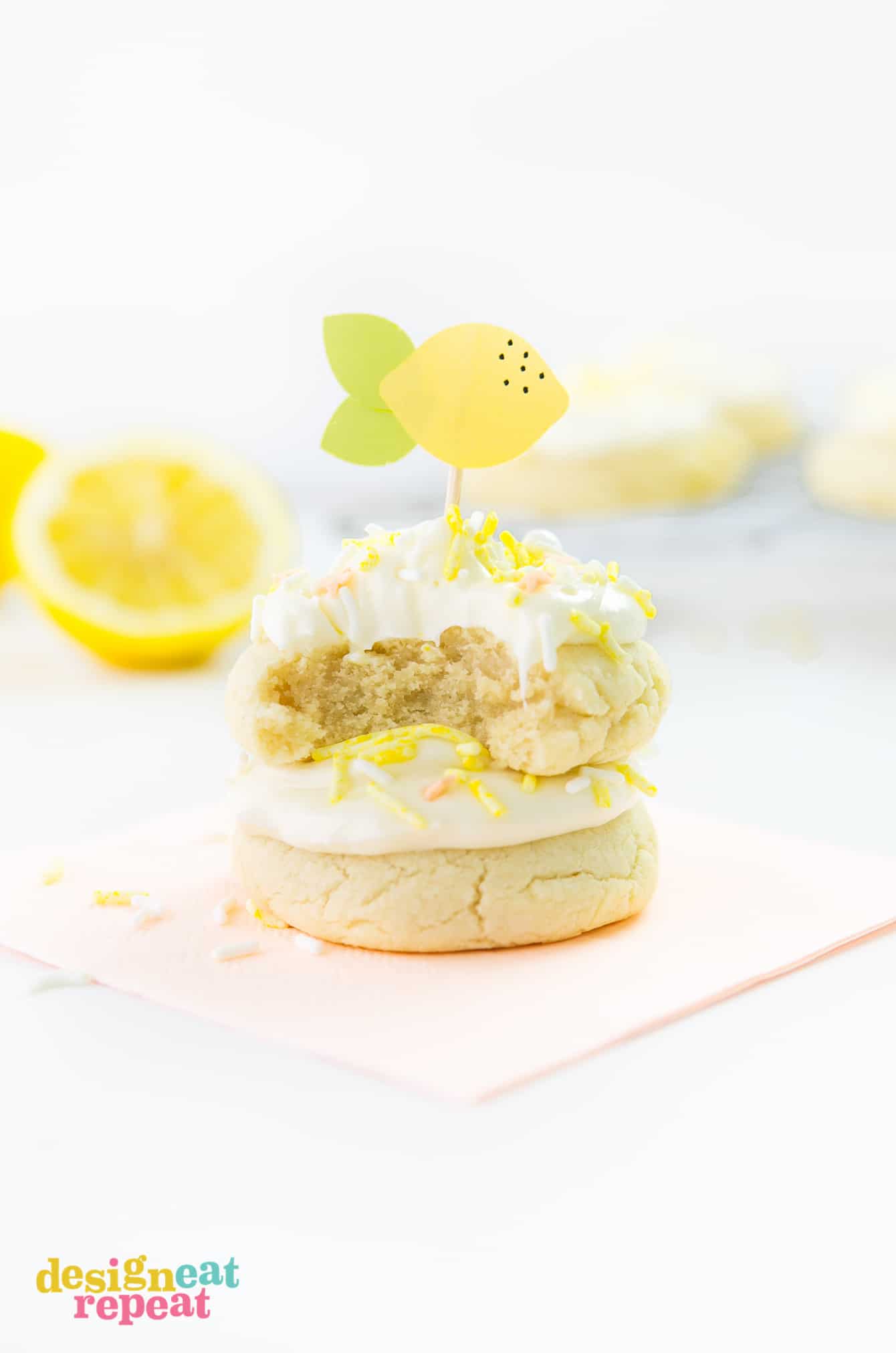 Stack of thick lemon sugar cookies with frosting, yellow sprinkles, and paper lemon toothpick topper on top.