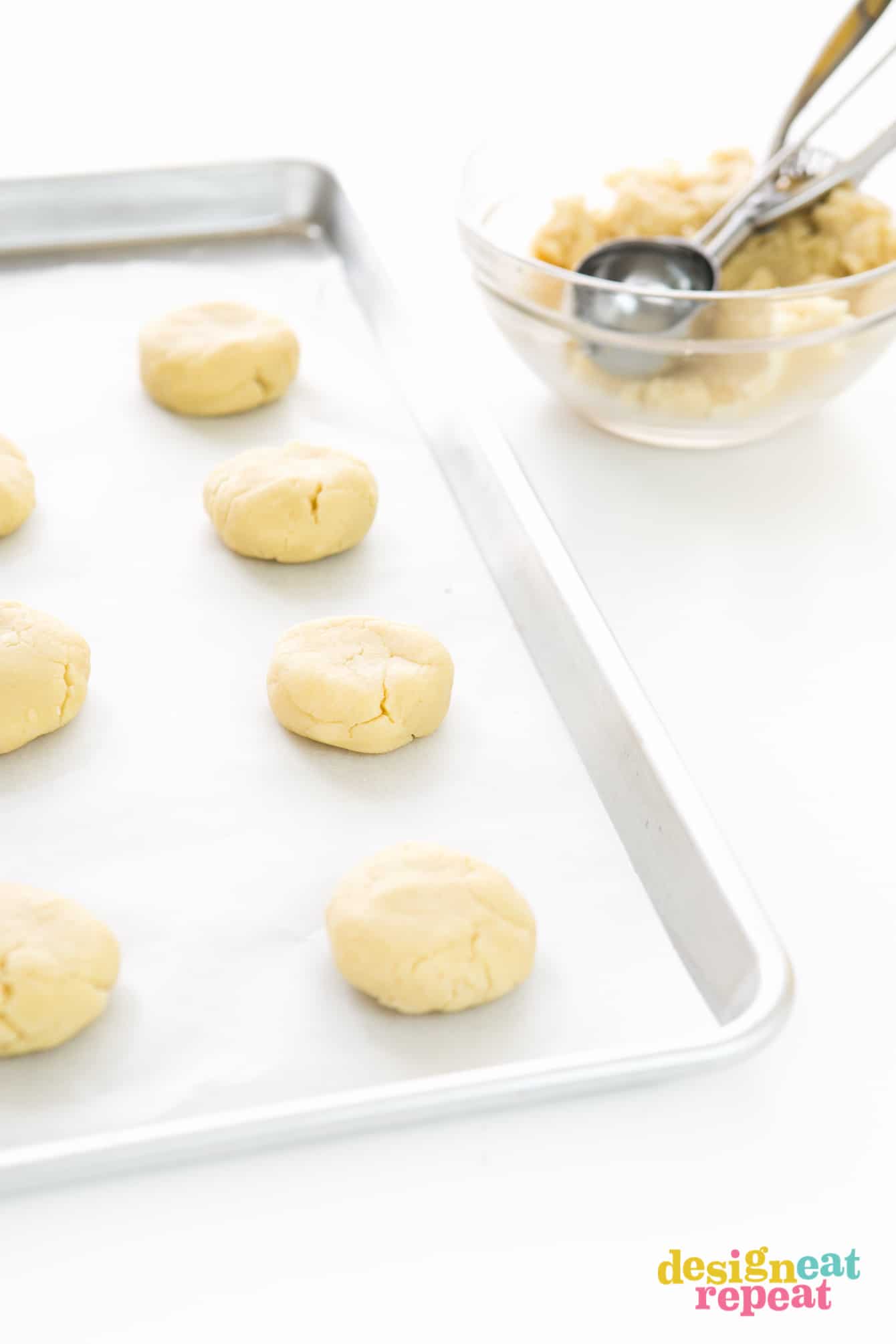 Tray of raw thick lemon sugar cookie dough being scooped into balls with metal scoop.
