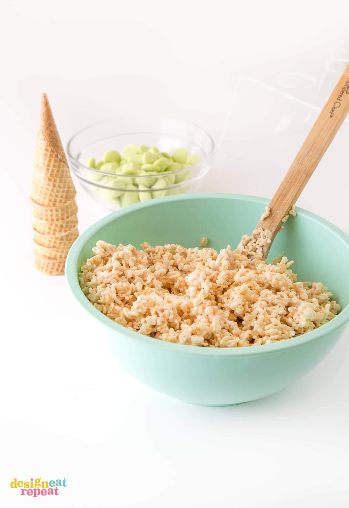 Mixing rice krispy cereal treats with wooden spoon in large blue bowl.